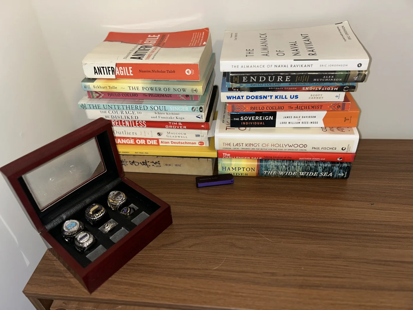 Stacks of books Noah has read beside an open wooden box holding rings he earned playing football.